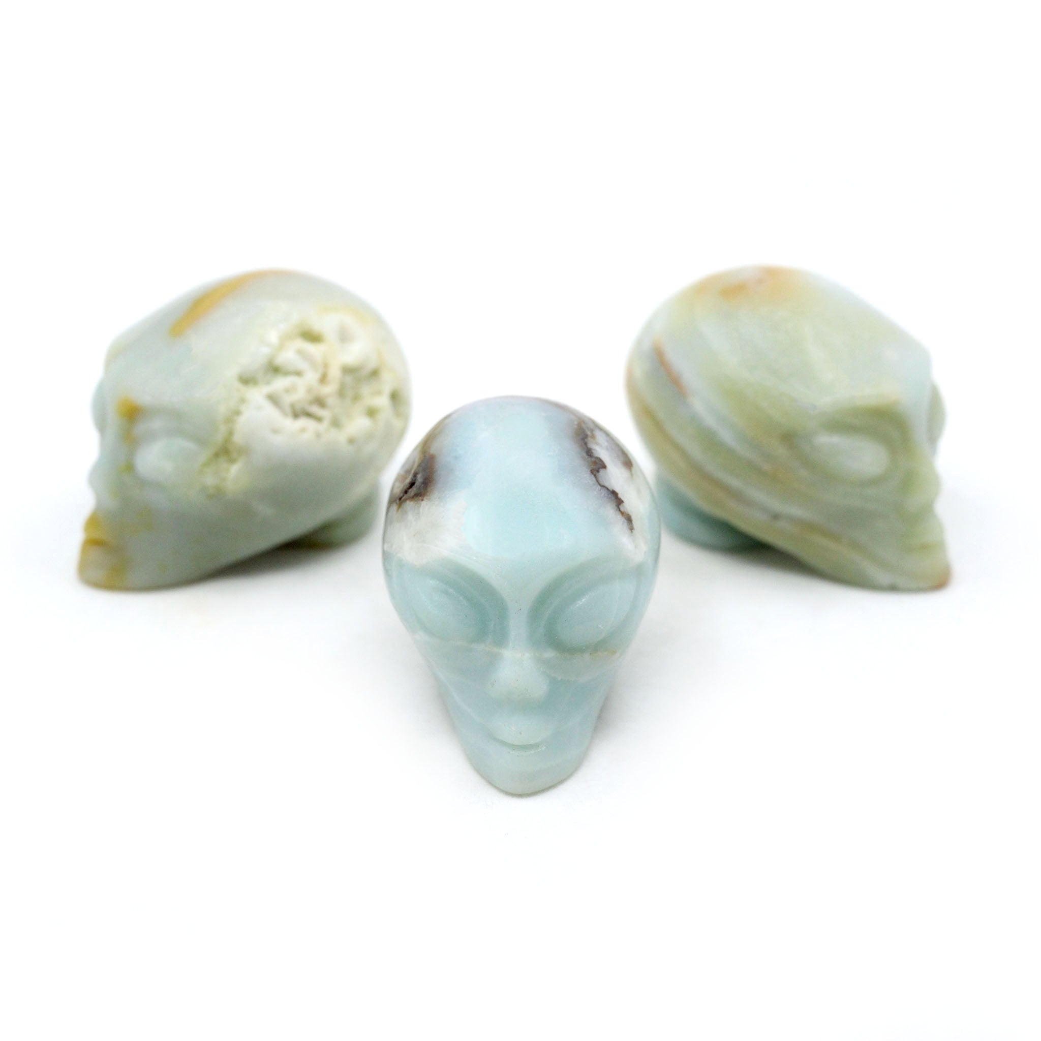 Three Alien heads carved from Amazonite on a white background