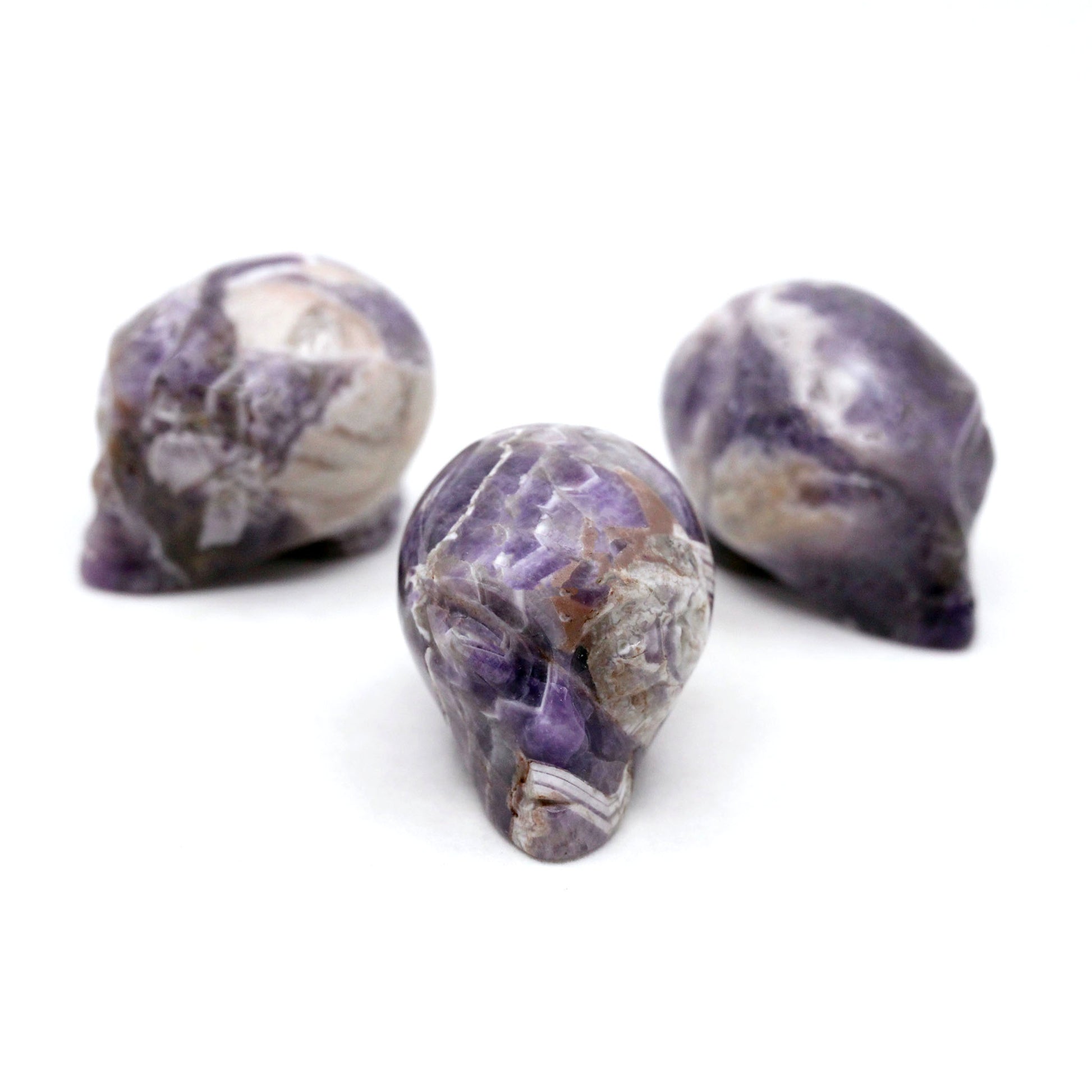 Three Alien heads carved from chevron  amethyst on a white background