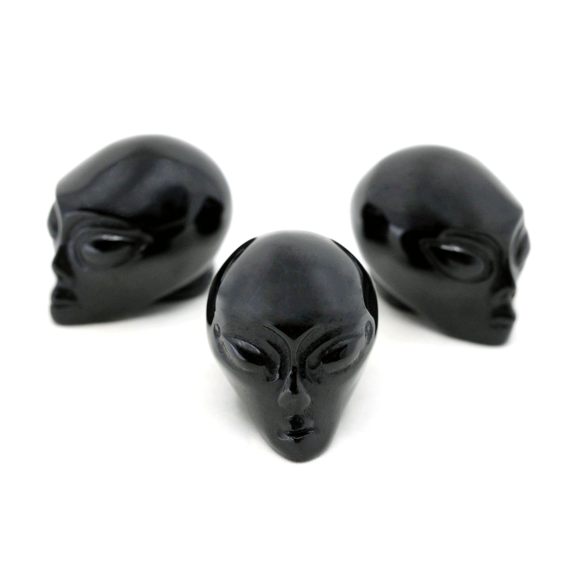 Three Alien heads carved from black obsidian on a white background