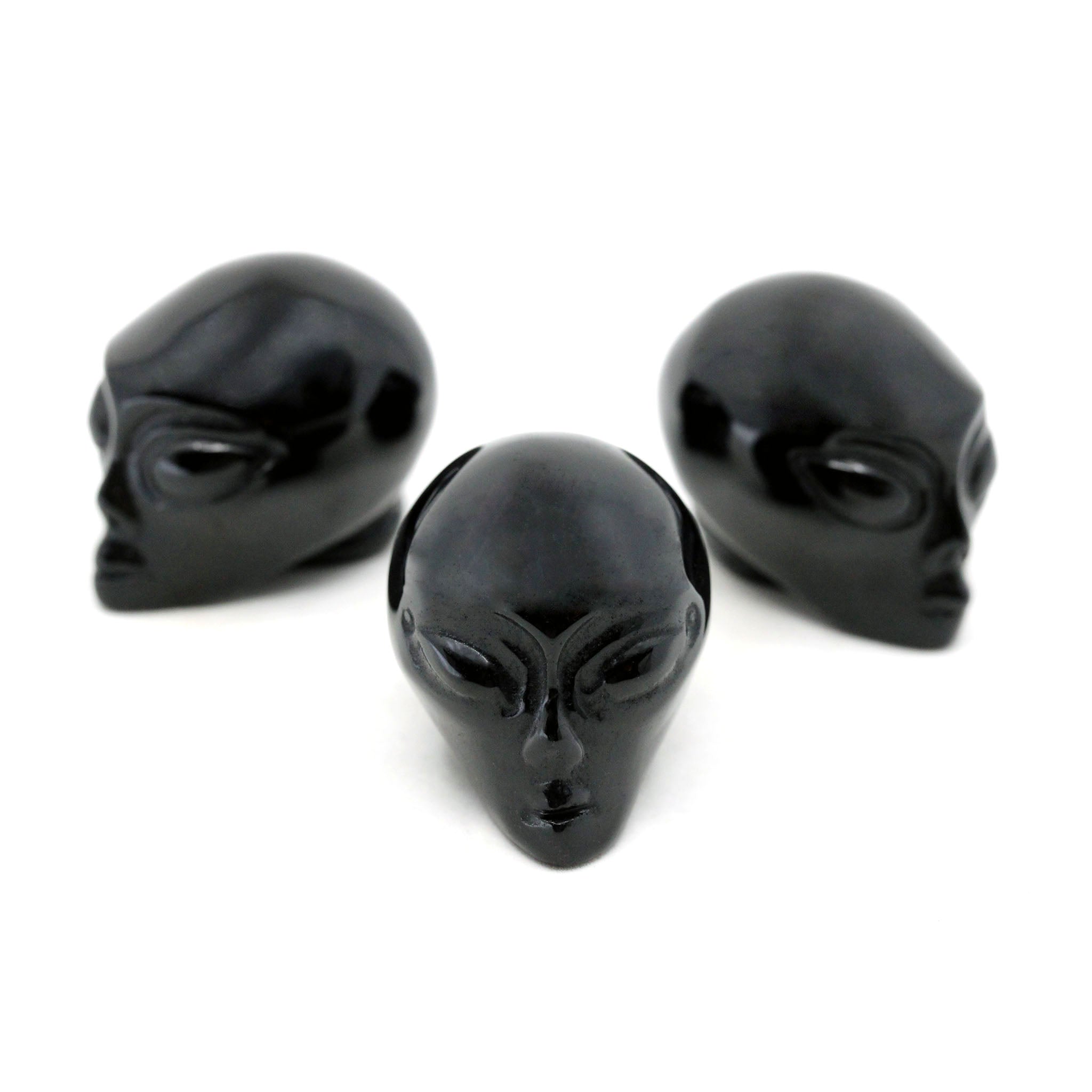 Three Alien heads carved from black obsidian on a white background