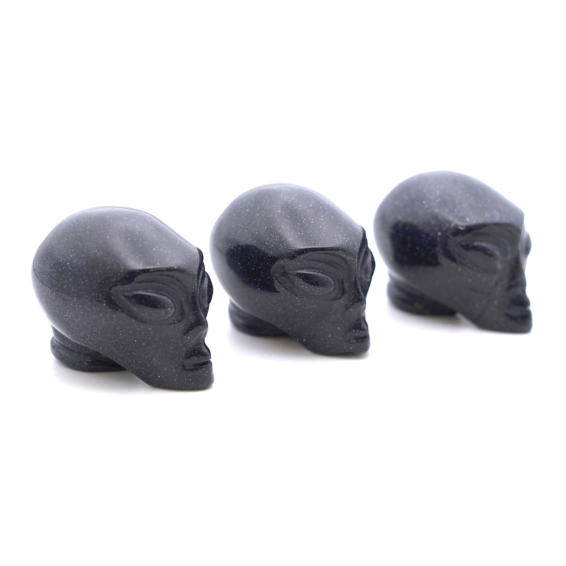 Three Alien heads carved from blue goldenstone on a white background