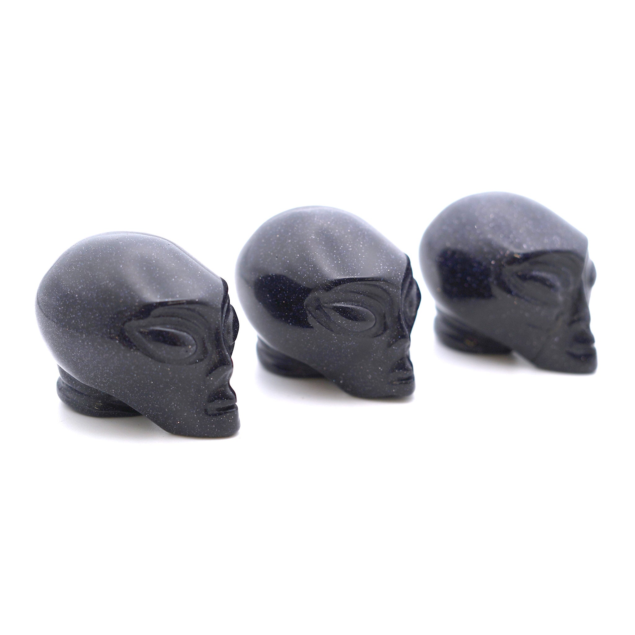 Three Alien heads carved from blue goldenstone on a white background