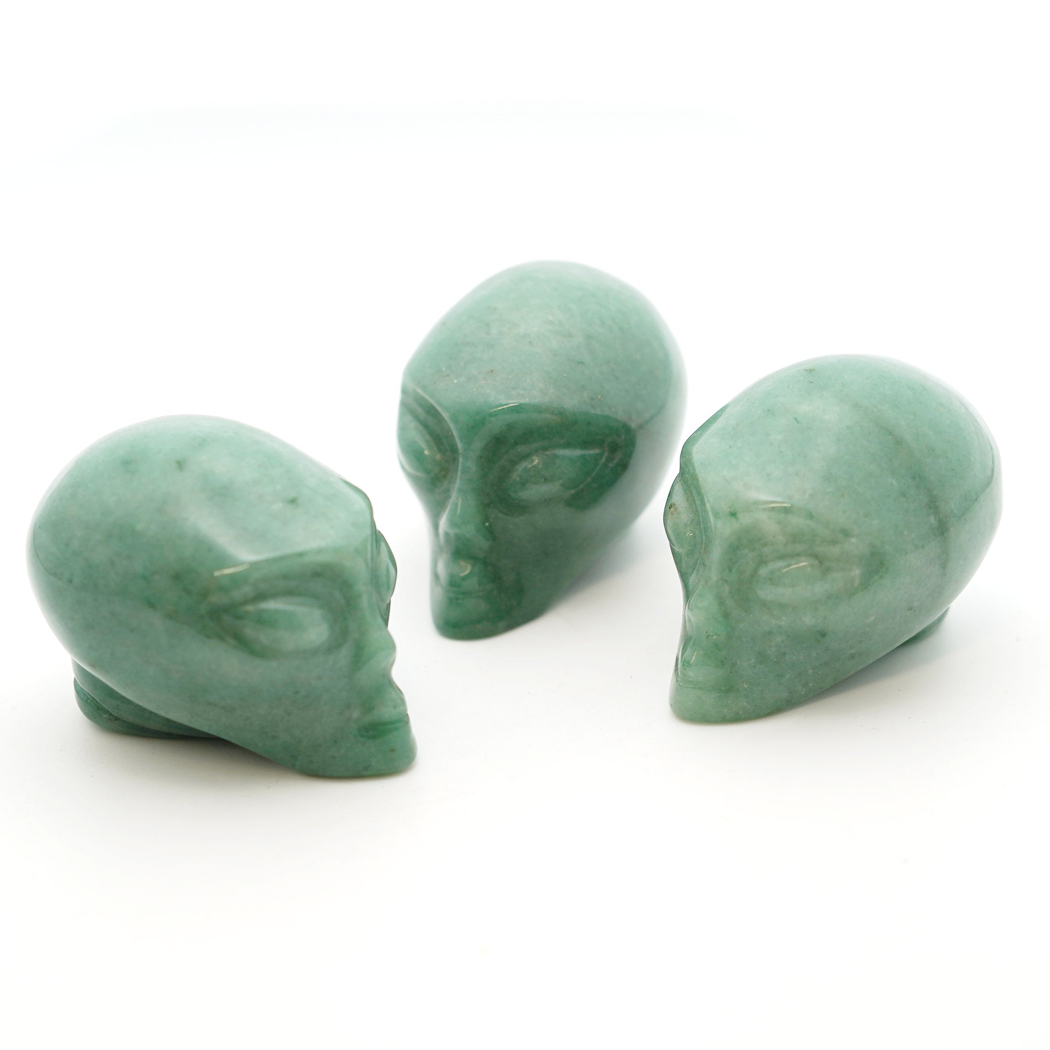 Three Alien heads carved from green aventurine on a white background