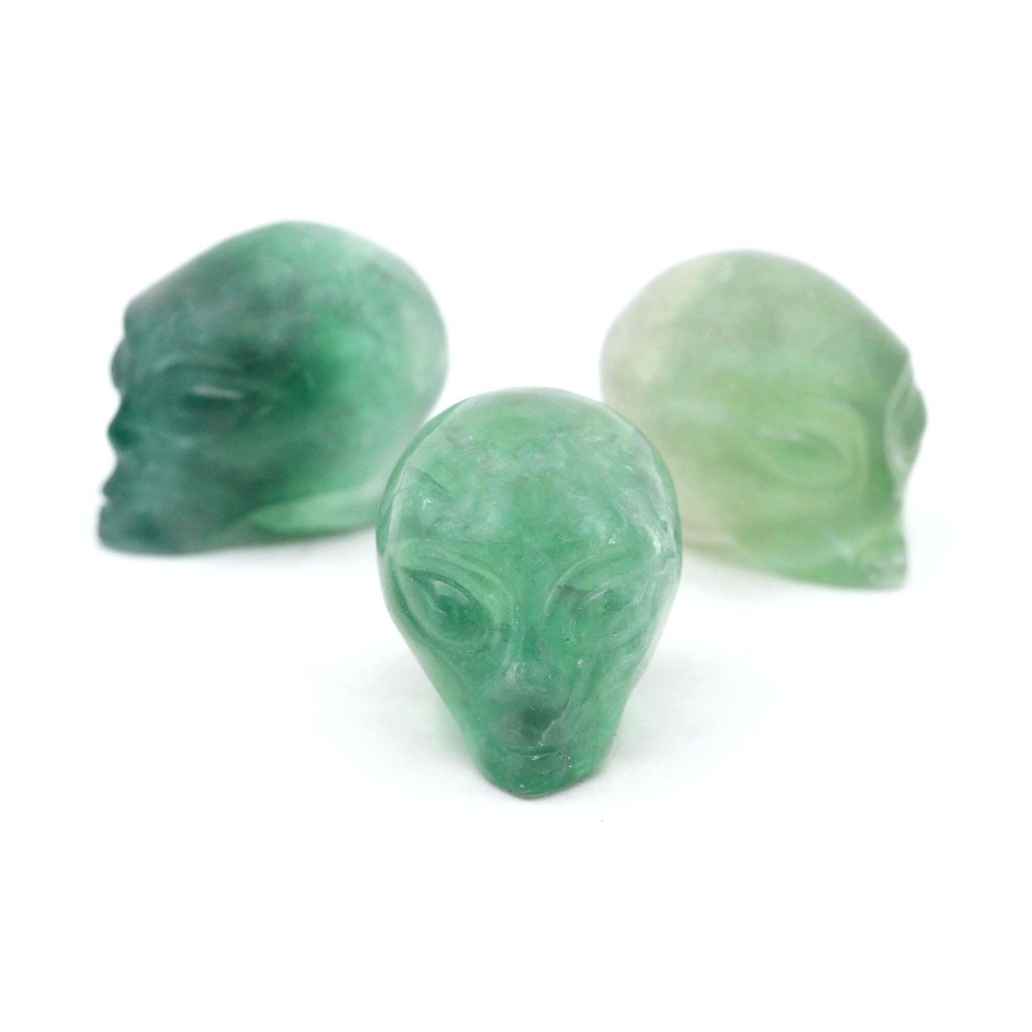 Three Alien heads carved from green fluorite on a white background