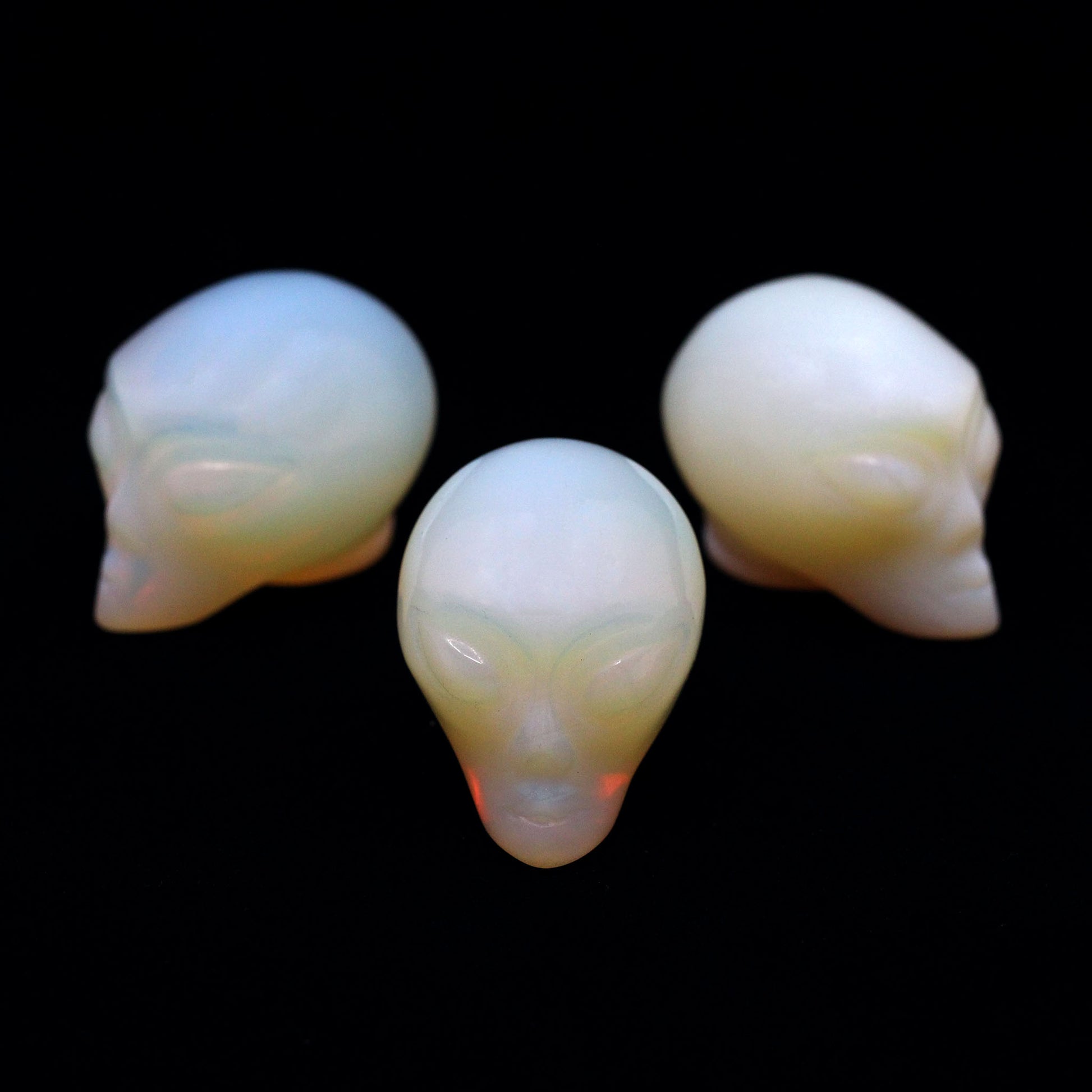 Three Alien heads carved from opalite on a black background