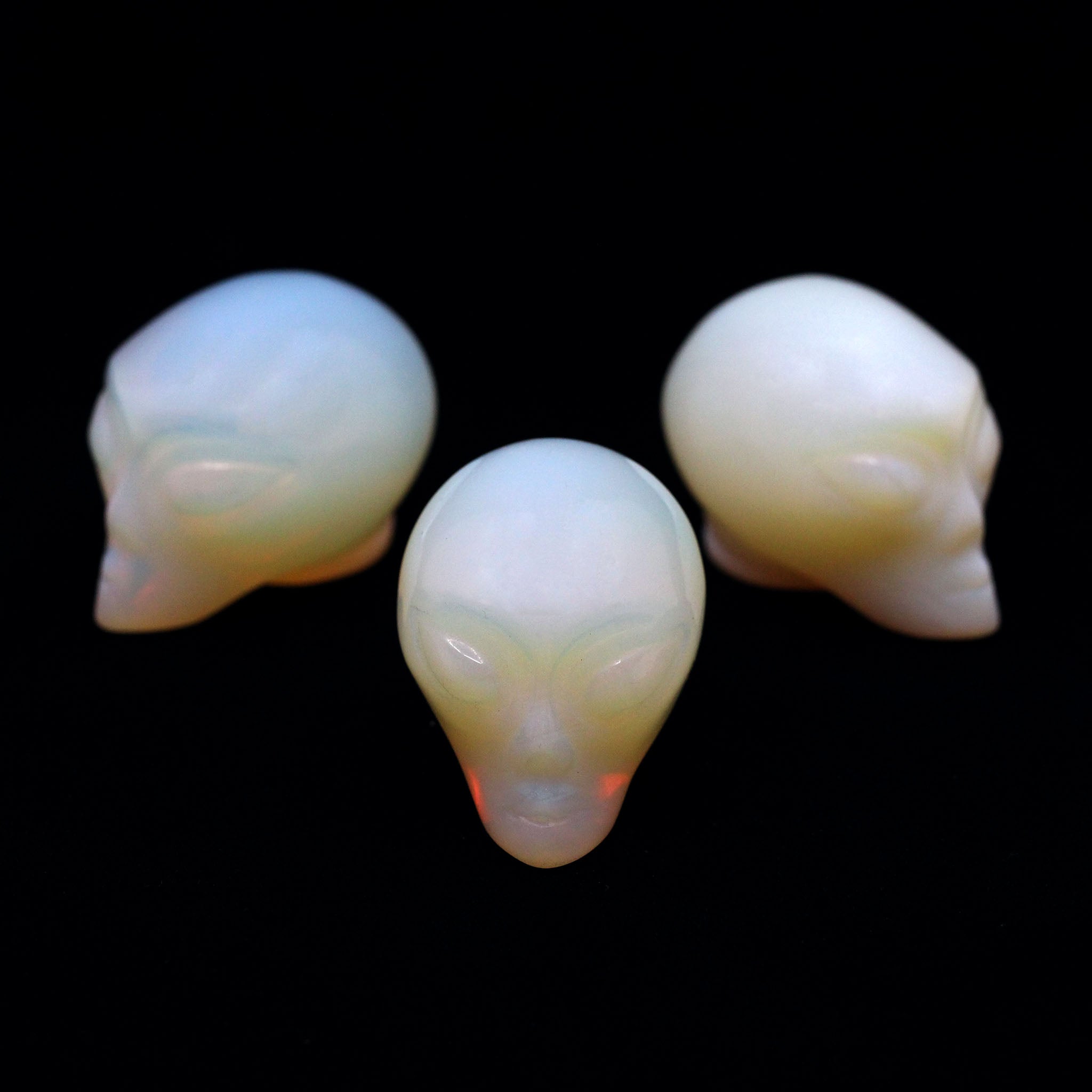 Three Alien heads carved from opalite on a black background
