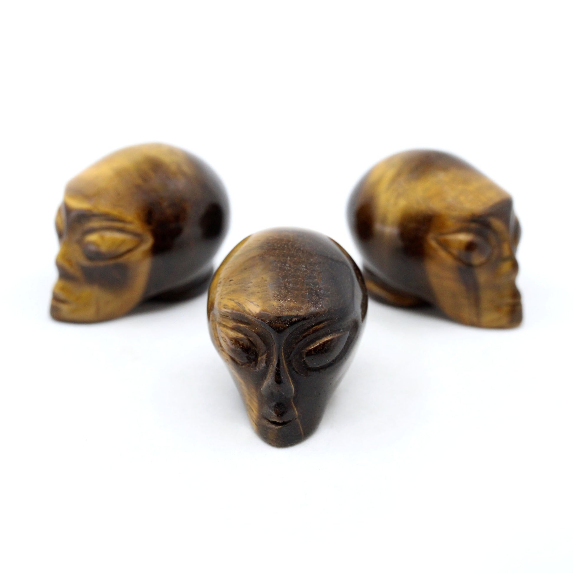 Three Alien heads carved from yellow tiger eye on a white background