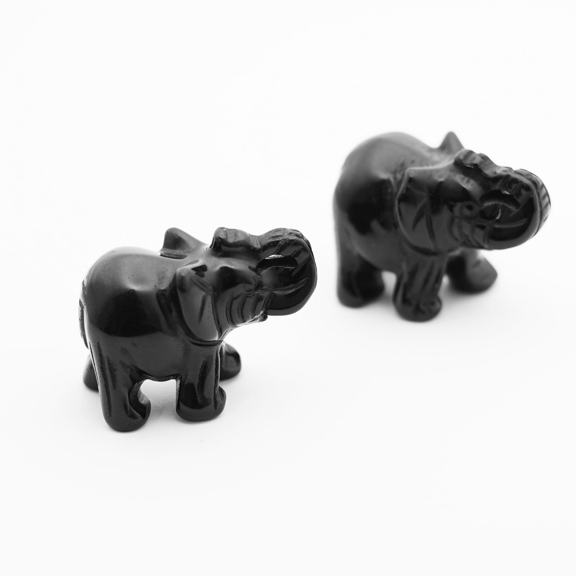 Two elephant figurines carved out of black obsidian on a white background