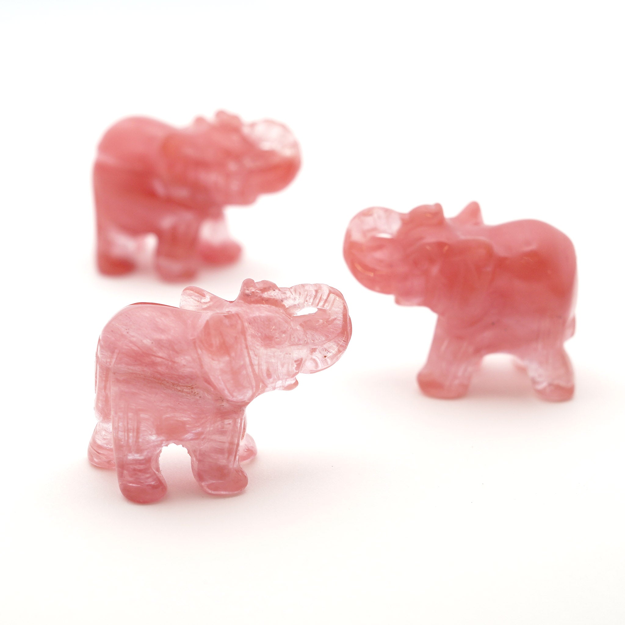 Three translucent red elephant figurines made from cherry quartz against a white background
