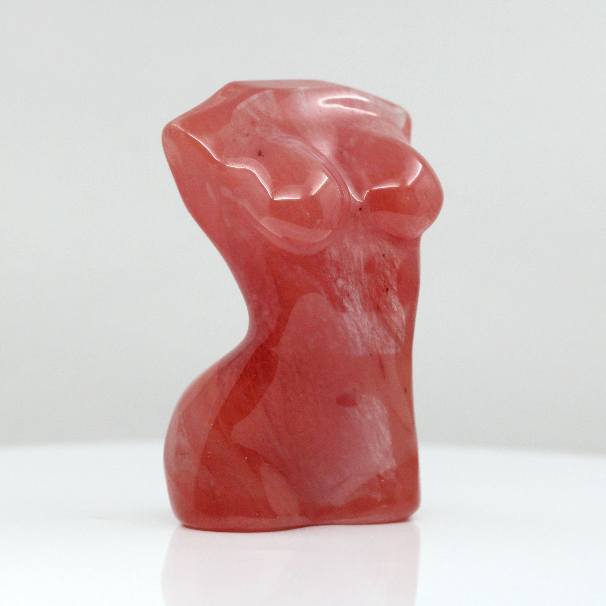 One sculpture in the shape of female body from neck down to upper thigh, with no arms, made from cherry quartz on a white background