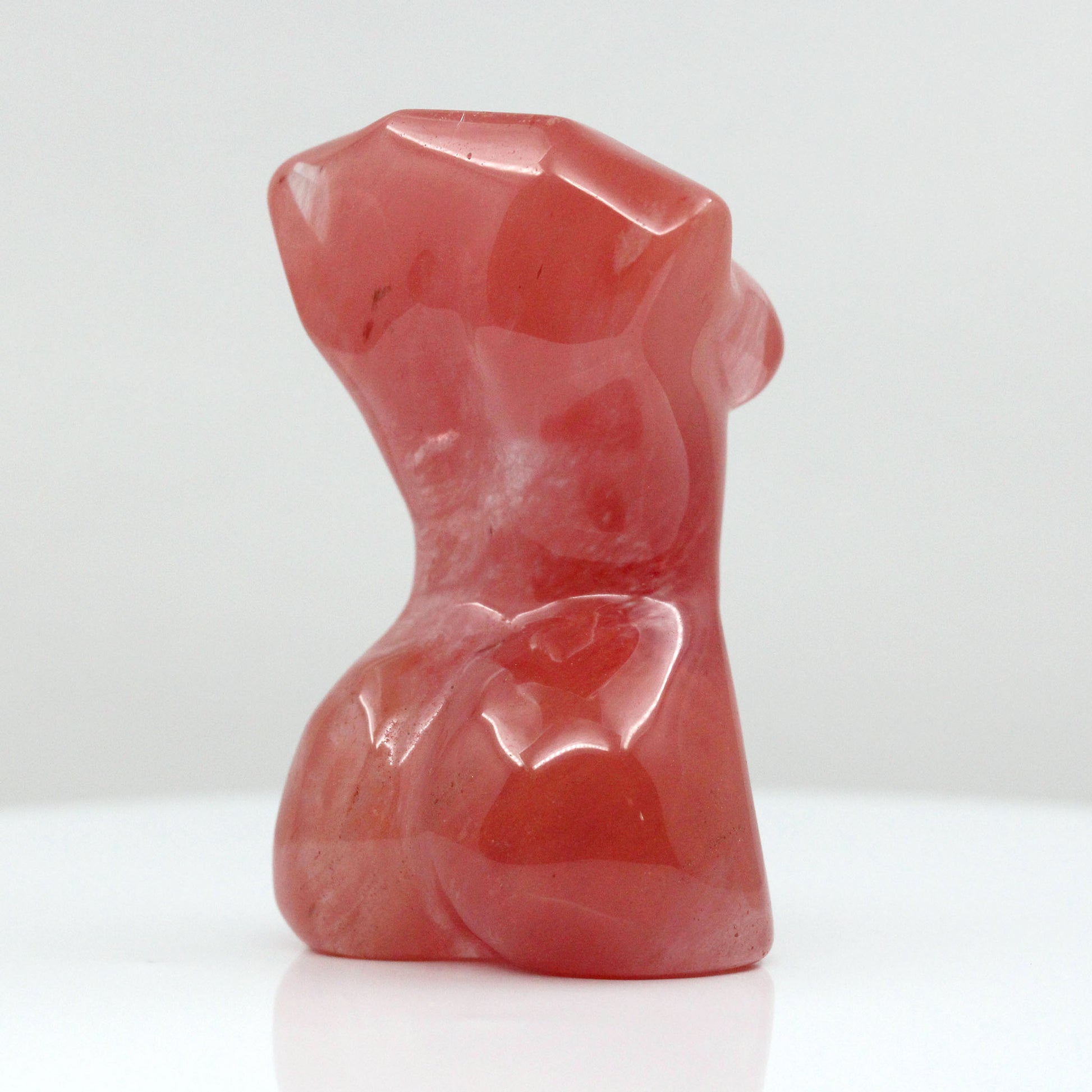 Backside of a sculpture in the shape of female body from neck down to upper thigh, with no arms, made from cherry quartz on a white background