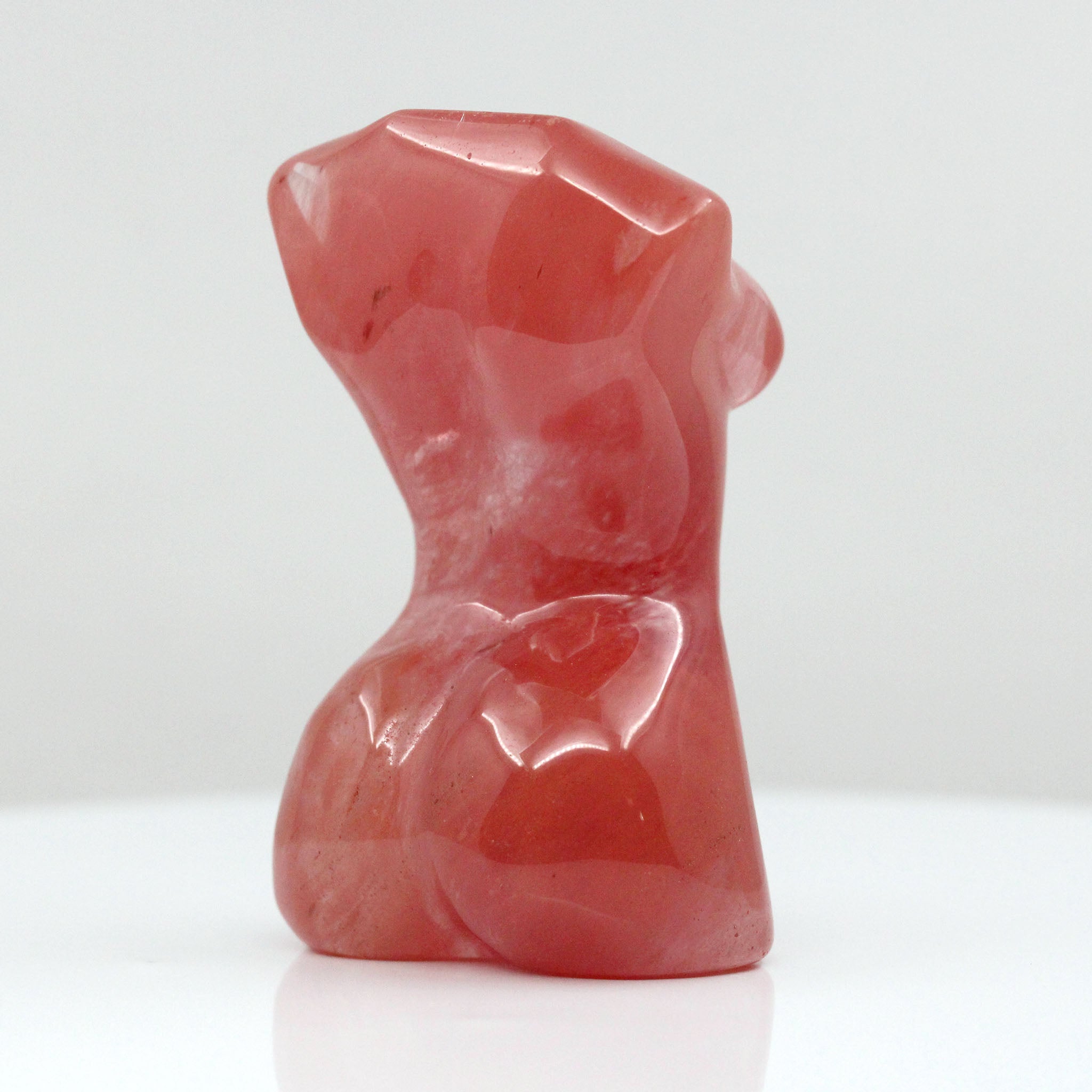 Backside of a sculpture in the shape of female body from neck down to upper thigh, with no arms, made from cherry quartz on a white background