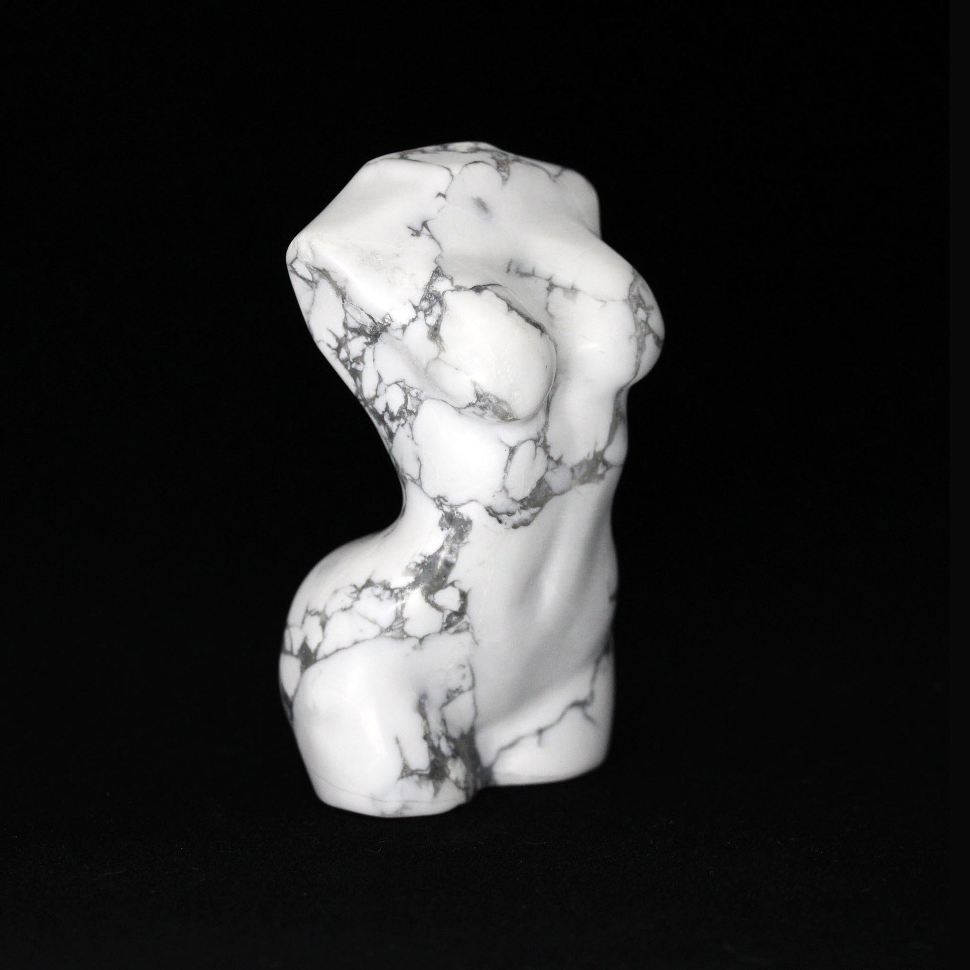 A sculptures in the shape of female bodies from neck down to upper thigh, with no arms, made from howlite, a white colored mineral with black veining, on a black background