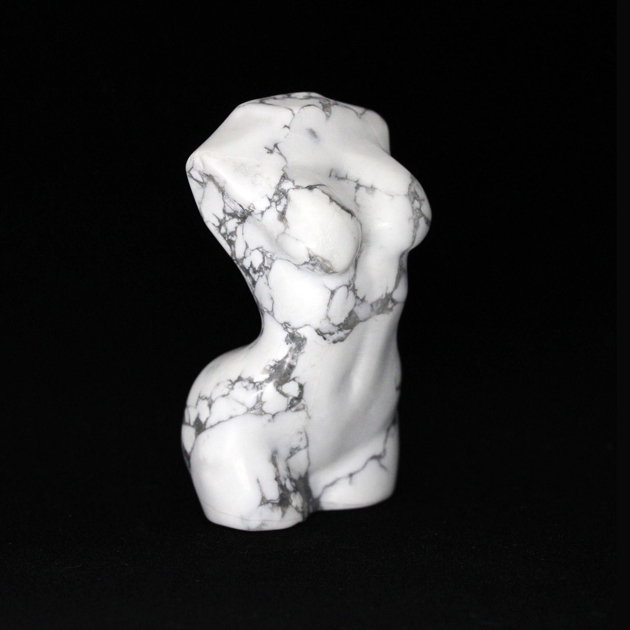 A sculptures in the shape of female bodies from neck down to upper thigh, with no arms, made from howlite, a white colored mineral with black veining, on a black background