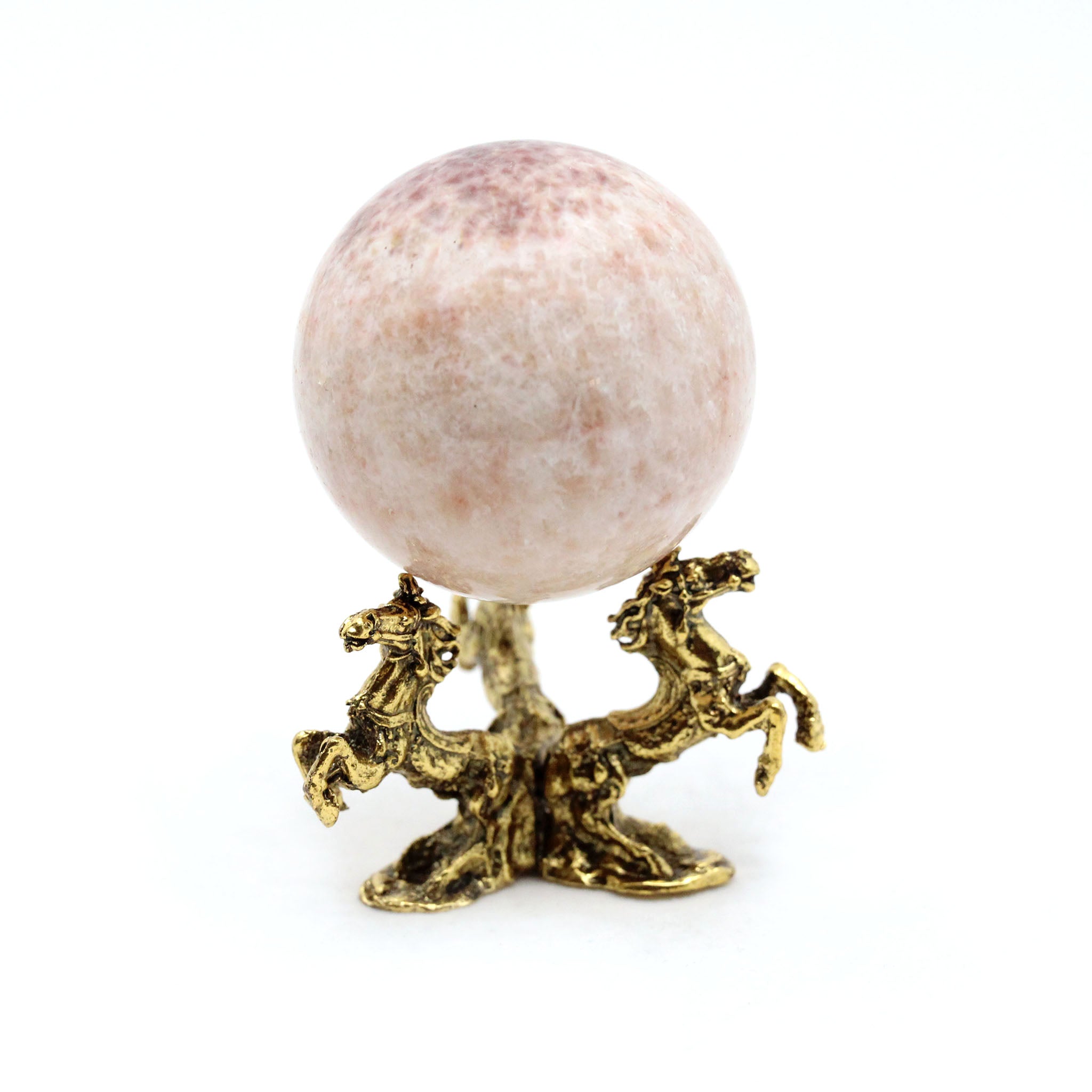 Decorative object with a pink sphere on a gold stand in the shape of three galloping horses against a white background