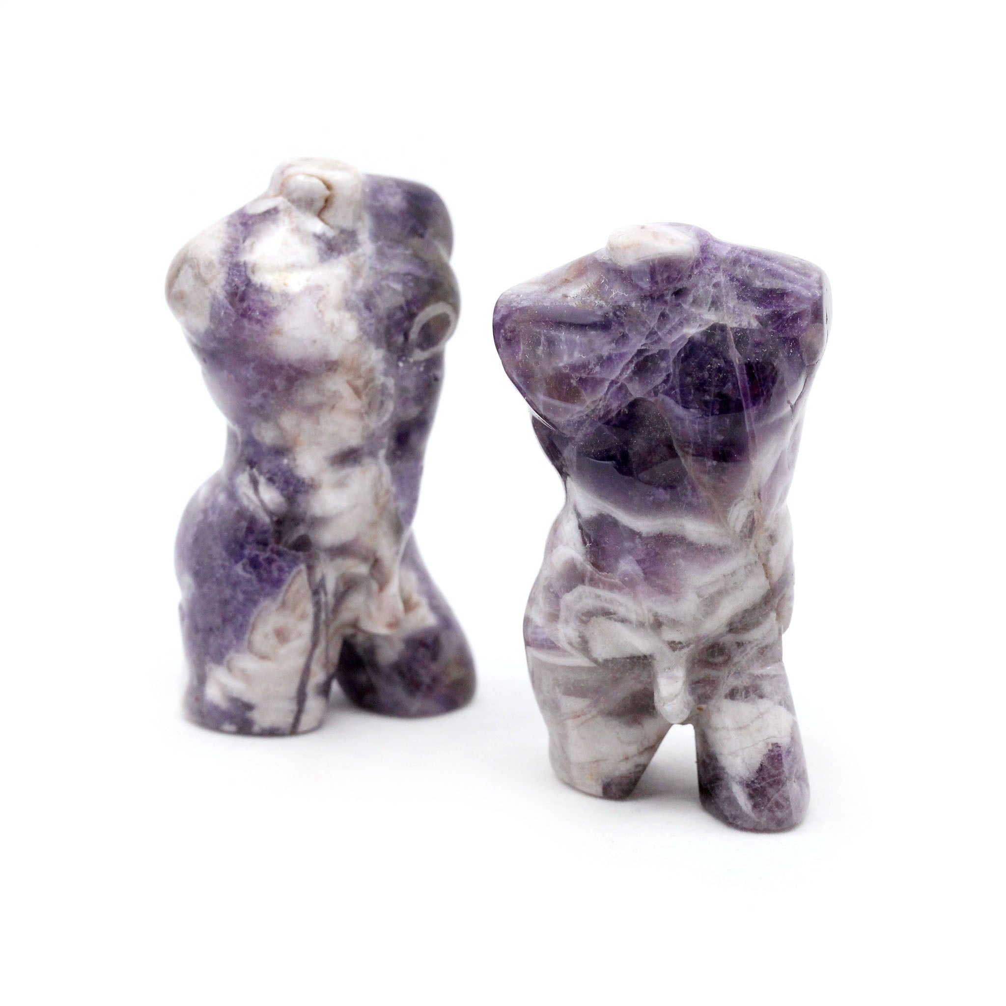 Two sculptures in the shape of male bodies from neck down to upper thigh, with no arms, made from amethyst, on a white background