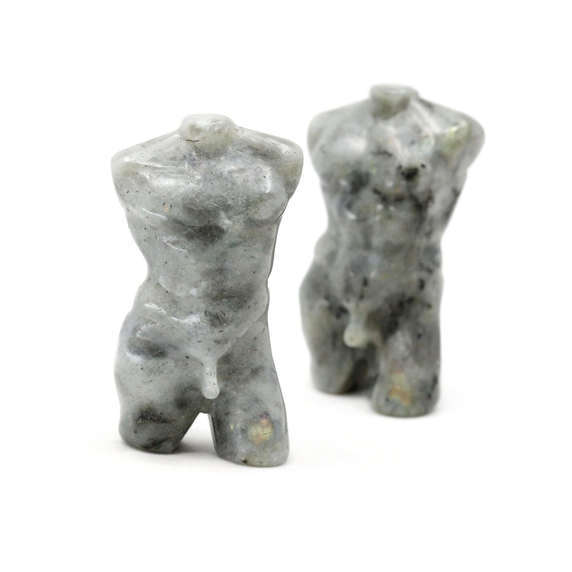 Two sculptures in the shape of male bodies from neck down to upper thigh, with no arms, made from labradorite, on a white background