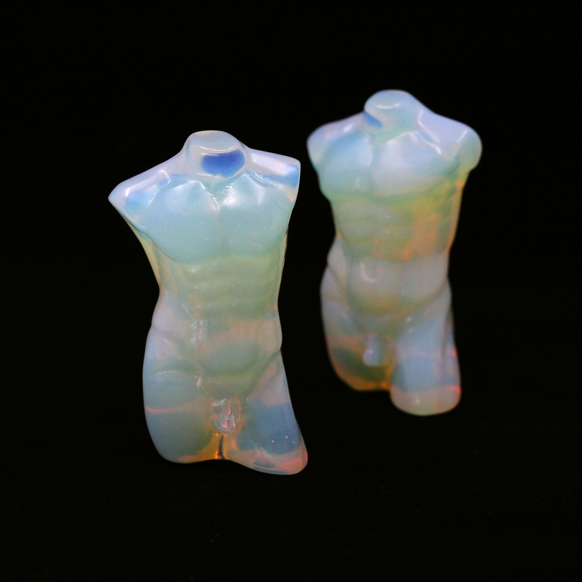 Two sculptures in the shape of male bodies from neck down to upper thigh, with no arms, made from opalite, on a black background