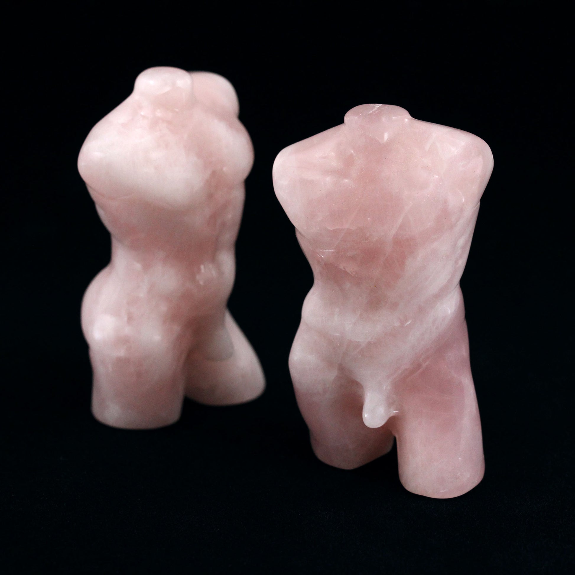 Two sculptures in the shape of male bodies from neck down to upper thigh, with no arms, made from rose quartz, on a black background