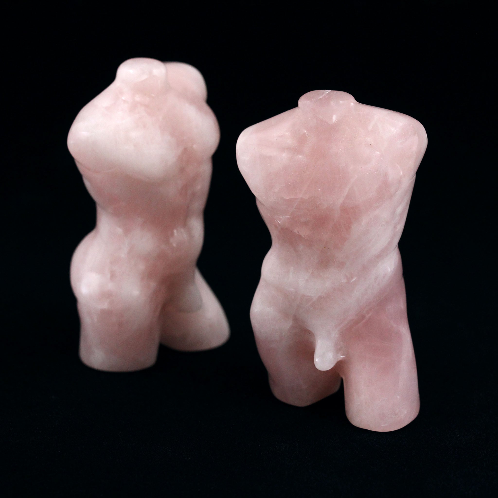 Two sculptures in the shape of male bodies from neck down to upper thigh, with no arms, made from rose quartz, on a black background