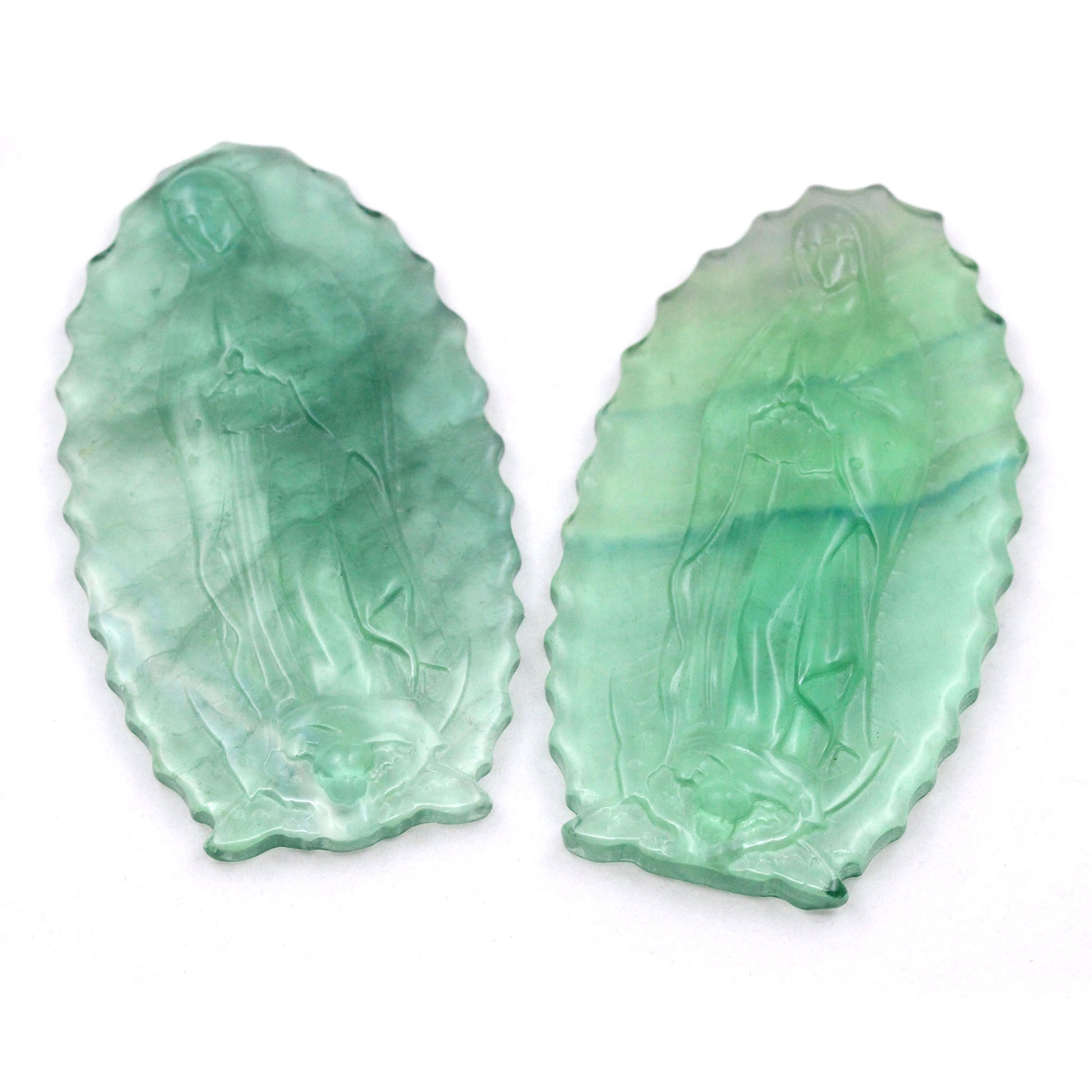 A photograph of two full body carvings of Our Lady of Guadalupe on pieces of green fluorite, against a white back ground.