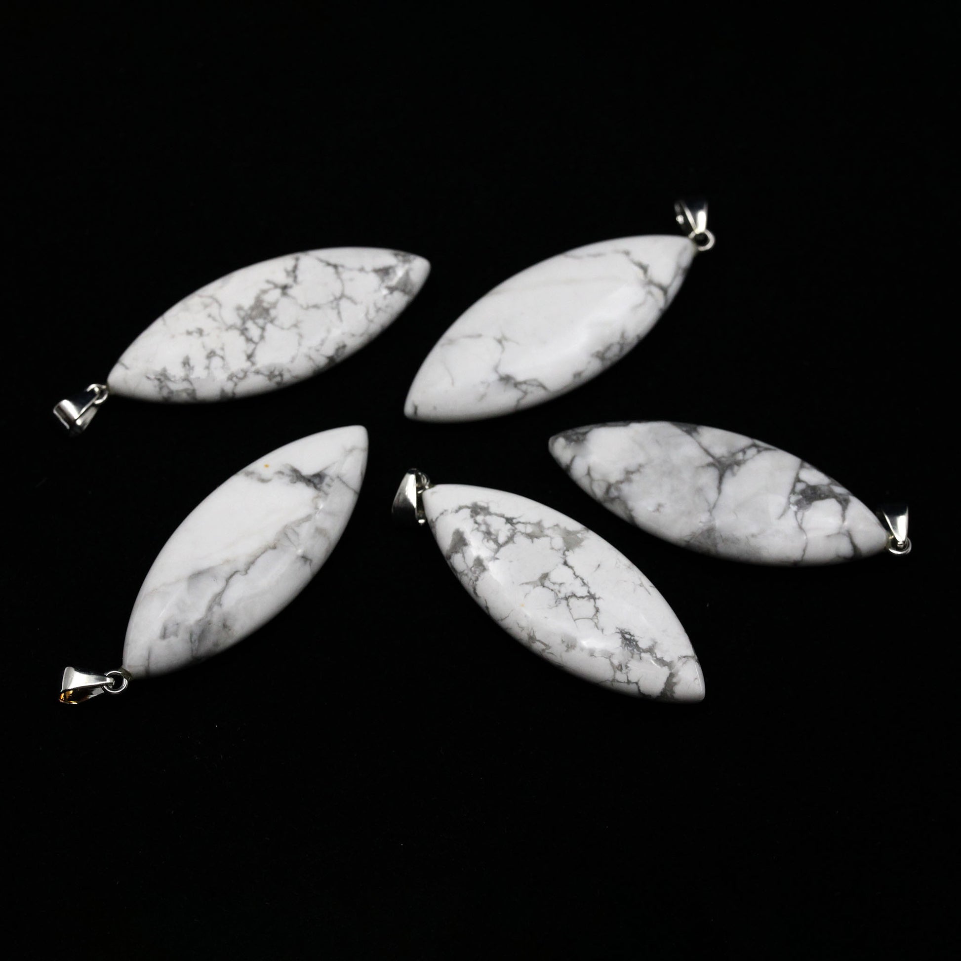 Five surfboard shaped pendants made from white Howlite on a white background. 