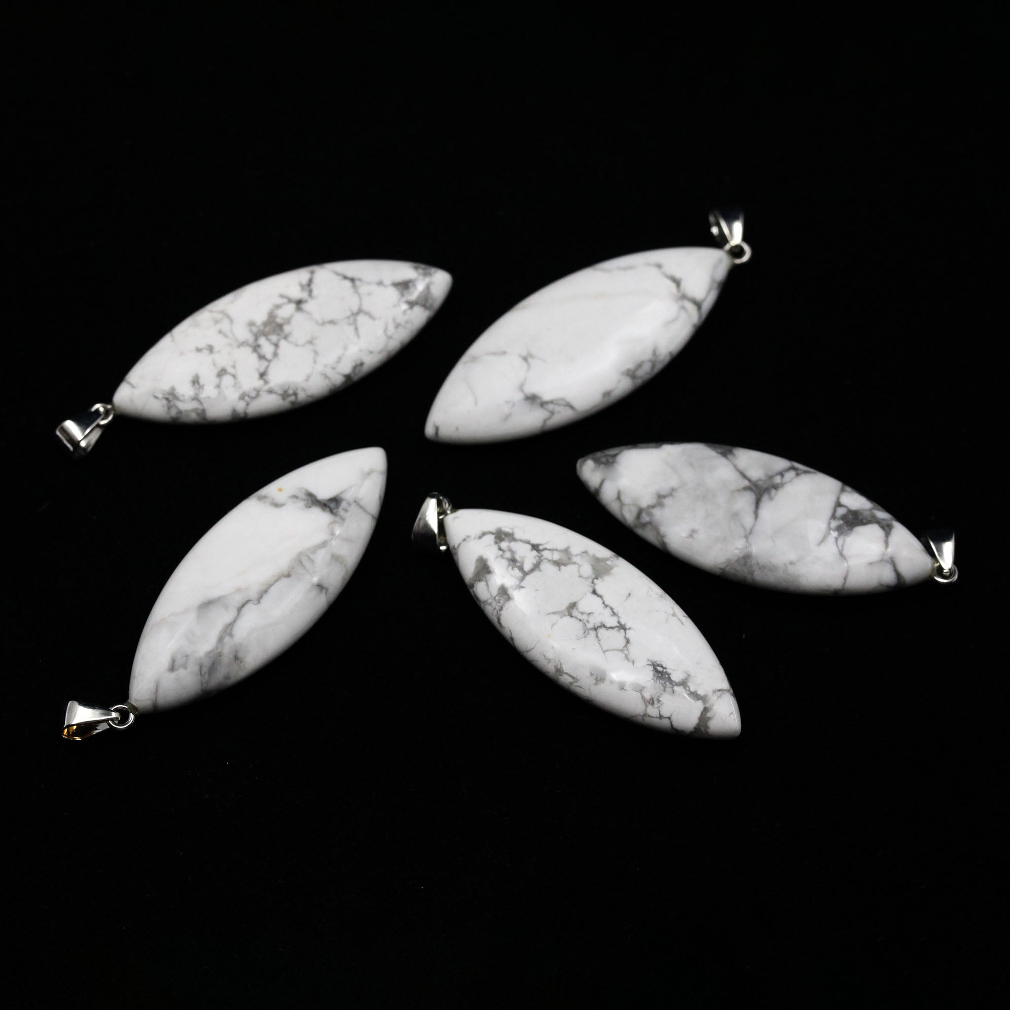 Five surfboard shaped pendants made from white Howlite on a white background. 