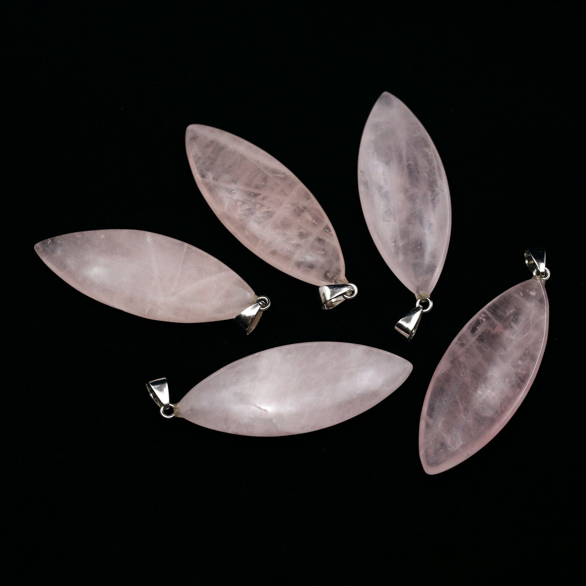 Five surfboard shaped pendants made from rose quarts on a black background