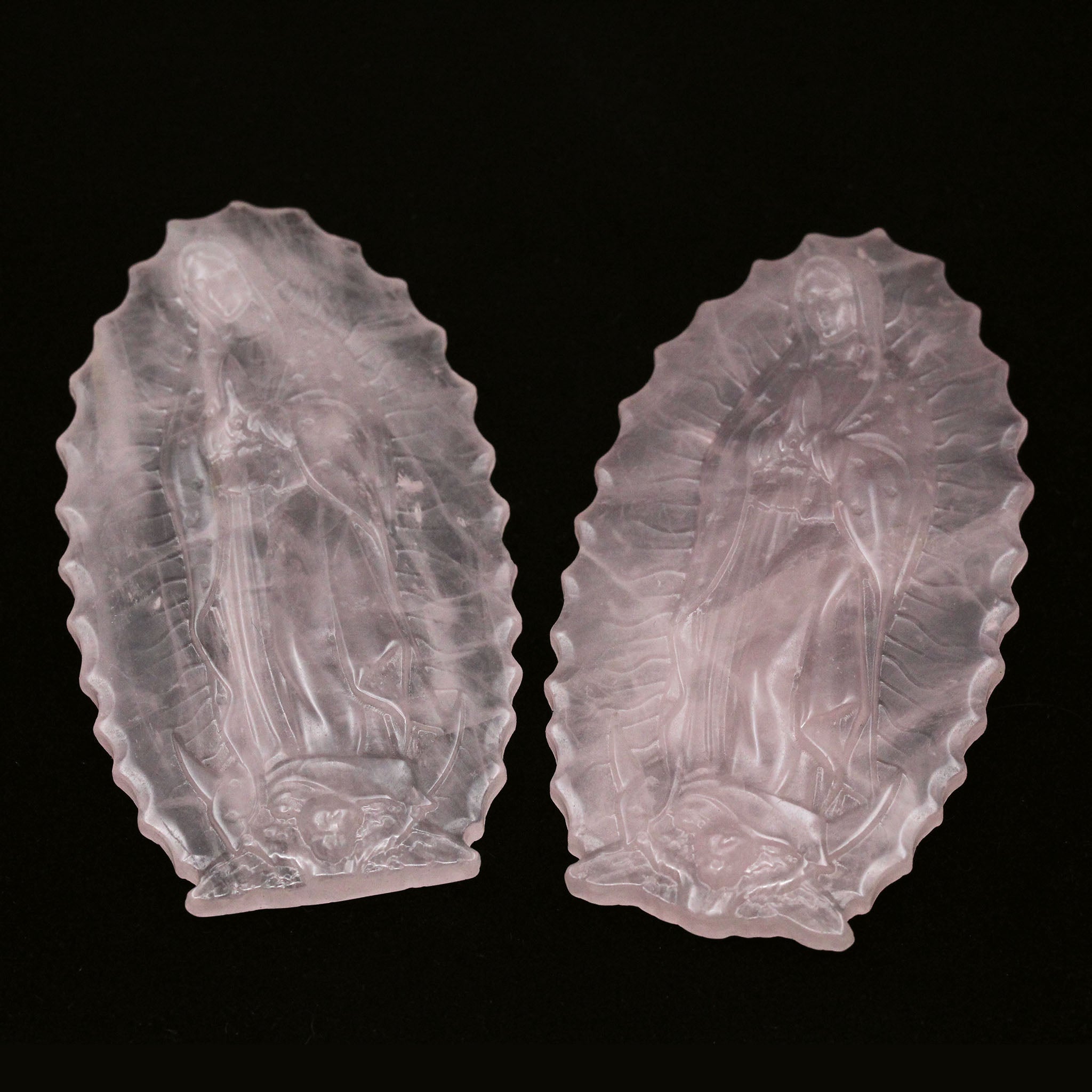 A photograph of two full body carvings of Our Lady of Guadalupe on pieces of rose quartz, against a white back ground.